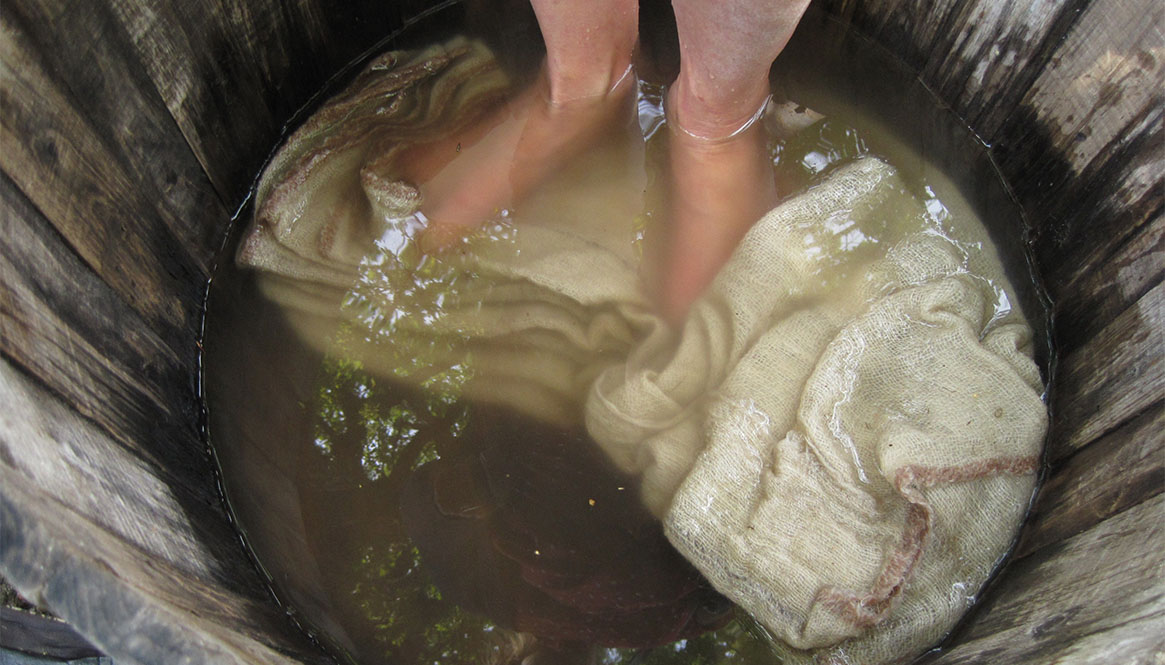 En balja med vatten där fötter stampar på ett vitt tyg.